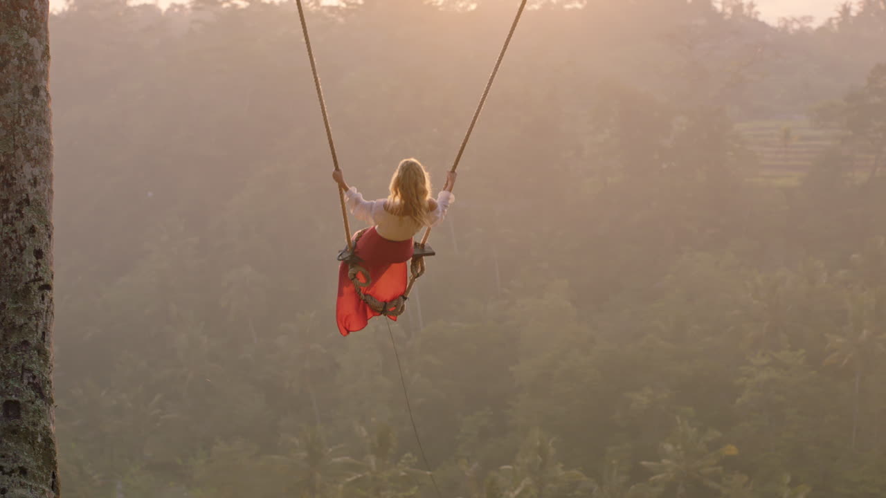 viajera mujer balanceándose sobre la selva tropical al amanecer turista mujer sentada en un columpio con una vista panorámica disfrutando de la libertad de vacaciones divirtiéndose estilo de vida de vacaciones cámara lenta