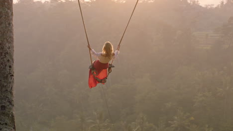 travel woman swinging over tropical rainforest at sunrise female tourist sitting on swing with scenic view enjoying freedom on vacation having fun holiday lifestyle slow motion