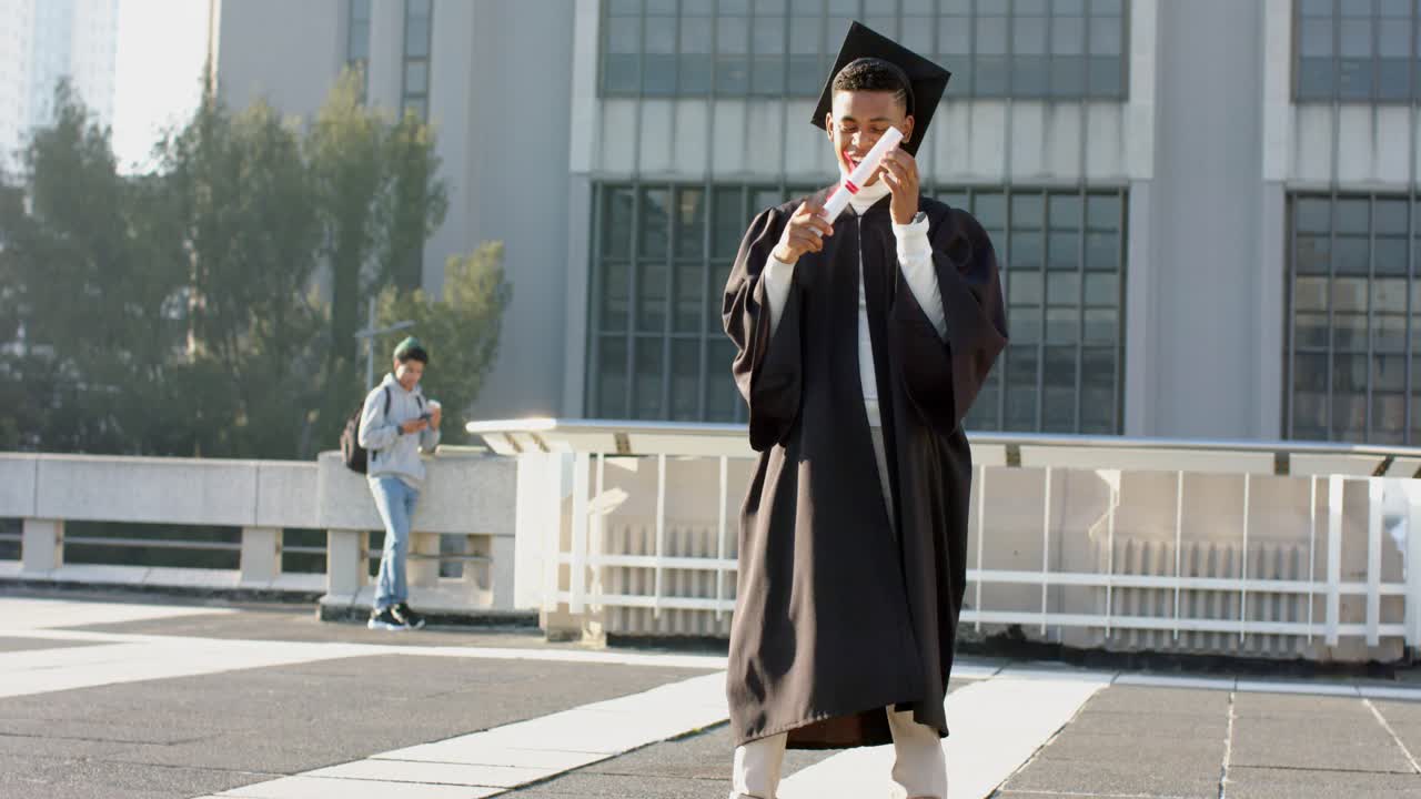 African American man graduate glancing at diploma, pumping fist, dancing on plaza, celebrating