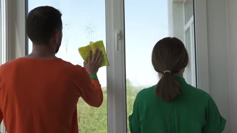 cleaning company workers in overalls are spraying detergent and wiping window panes in a city apartment. washing windows with a spray bottle.