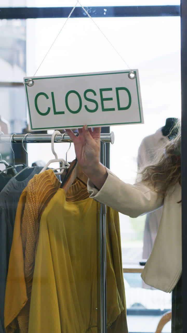Donna che gira il cartello da 'Aperto' a 'Chiuso' in un negozio di abbigliamento