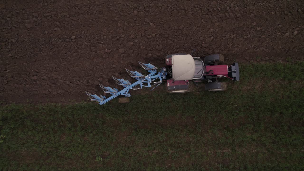 Top down of an older tractor plows a field in spring on a cloudy day