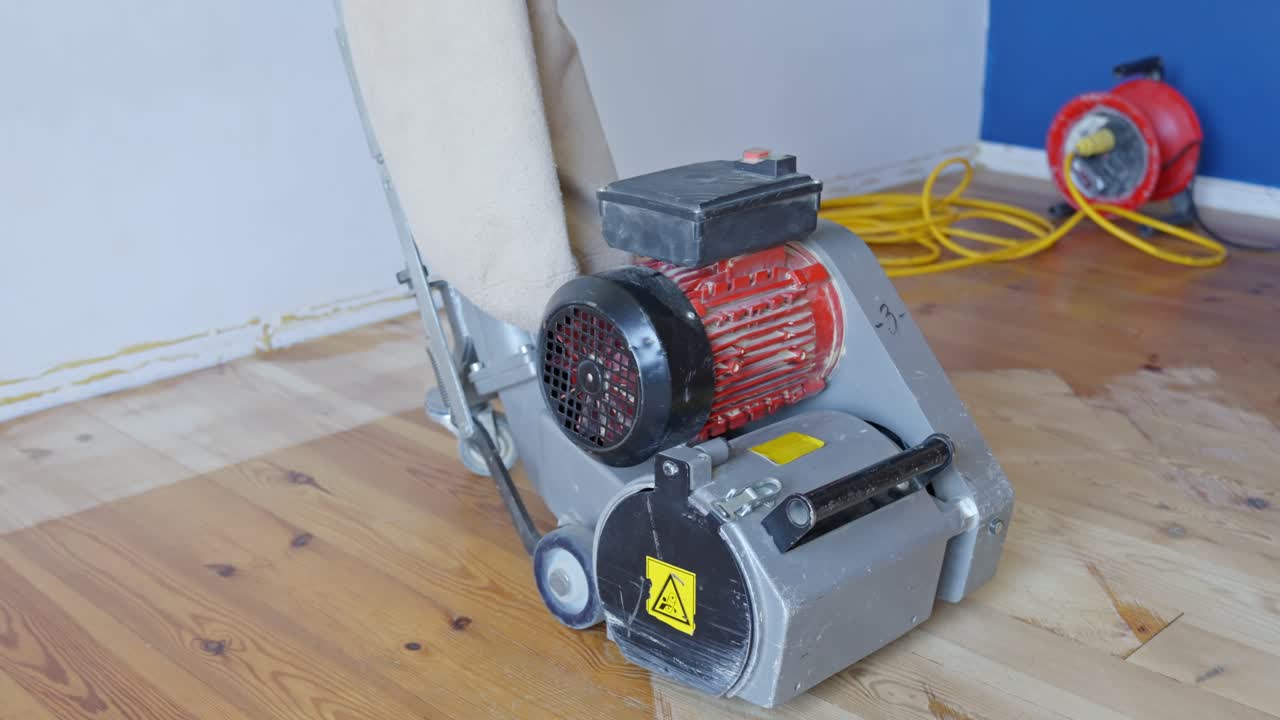 Floor sanding machine standing idle in renovated corner of a room with extension cord