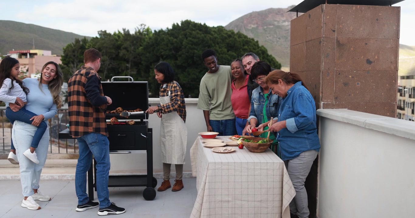 Famiglia e amici multigenerazionali e multietnici felici che si godono una festa barbecue in terrazza.