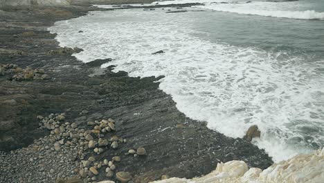 olas en cámara lenta que llegan sobre una playa oscura y rocosa en un día de verano nublado