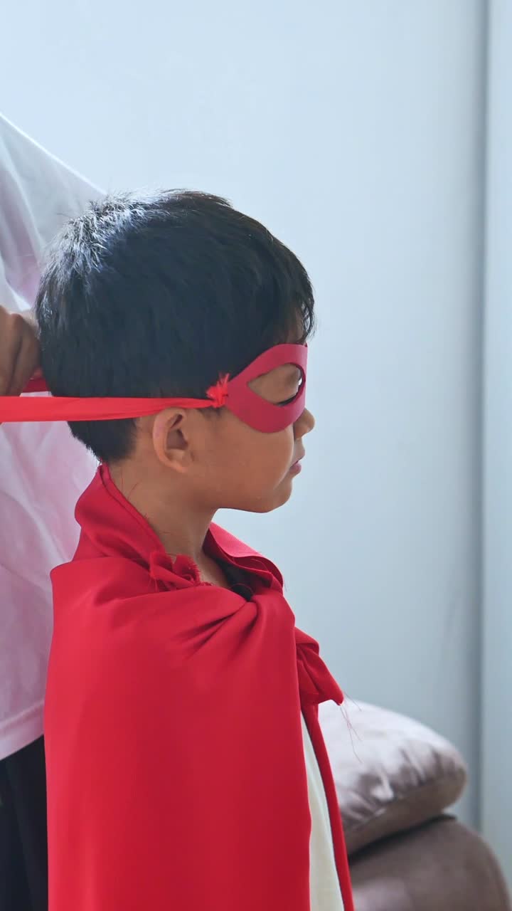Close up Older brother helps younger sibling dress as superhero at home