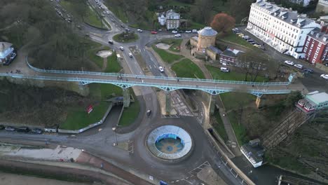 fotografía cinematográfica de un pie azul metálico sobre un puente con algunos transeúntes durante un día de invierno en la bahía de scarborough, inglaterra