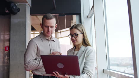 two people at work discussing something on computer and smiling. woman holds a laptop and asks her male colleague about some issues.