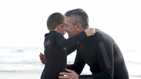 father and son in wetsuits hugging on beach