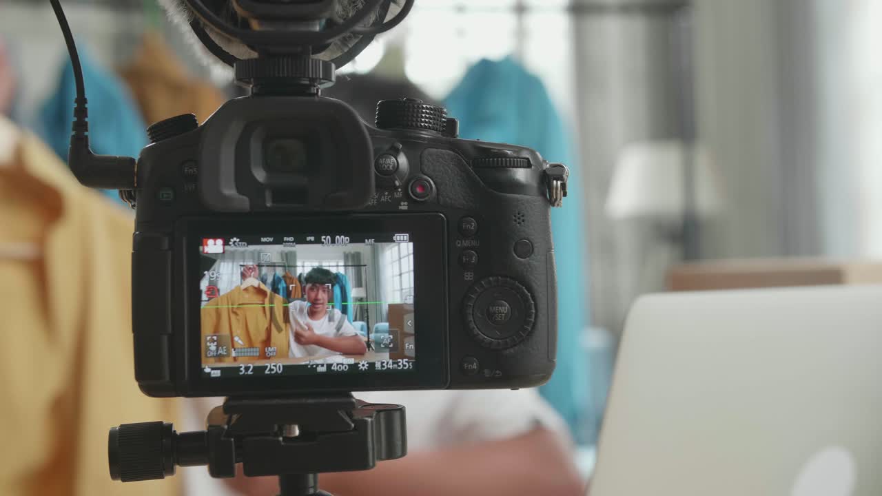 close up de un monitor de cámara grabando a un joven asiático vendedor en línea recomendando una camisa mientras usa la computadora para vender ropa en casa