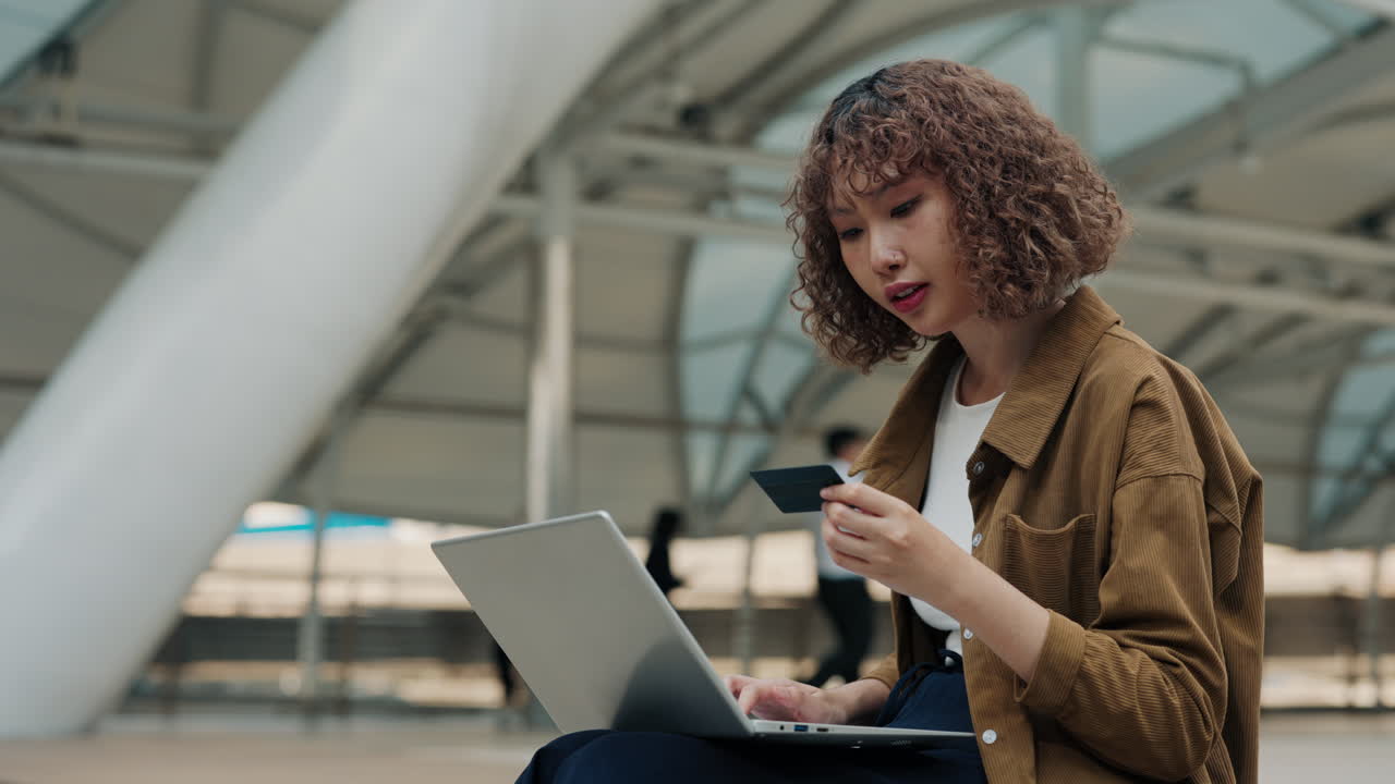 Woman using laptop and credit card outdoors
