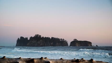 gorgeous landscape beach shot of driftwood with waves crashing in the background, a beautiful small cliff island, and a colorful cloudy sky during sunset at the famous ruby beach in forks, washington