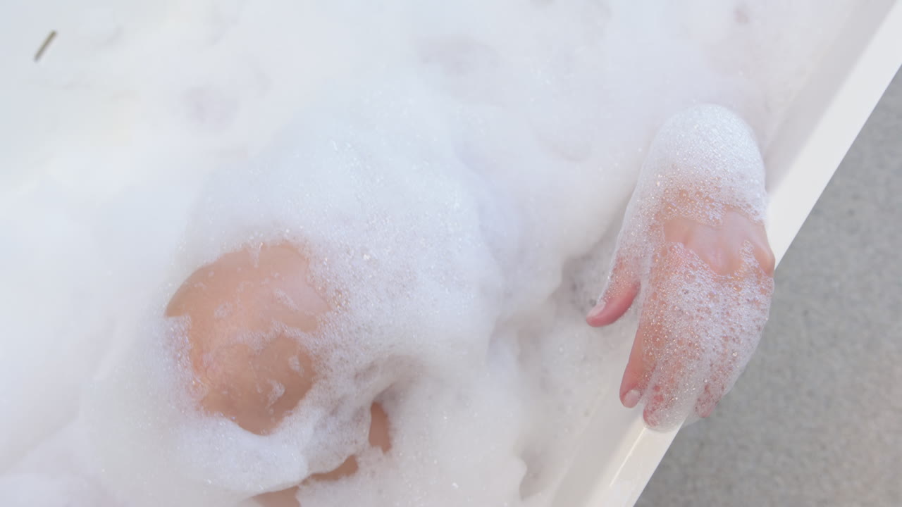 Relaxing in bathtub, woman enjoying bubble bath with hands visible, copy space