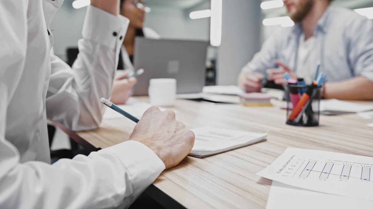 노트북에 정보를 기록하는 알 수 없는 직원의 손, 사무실에서 비즈니스 회의를 하는 다양한 동료