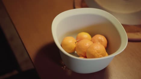 close up view man picks oranges in a basket and takes one from the white basket and kept it again in that basket which is on a wooden table