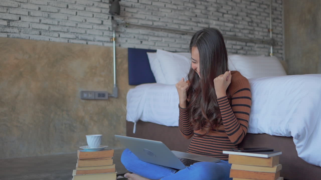 Successful woman at home surrounded by books, using laptop, rise hands cheering