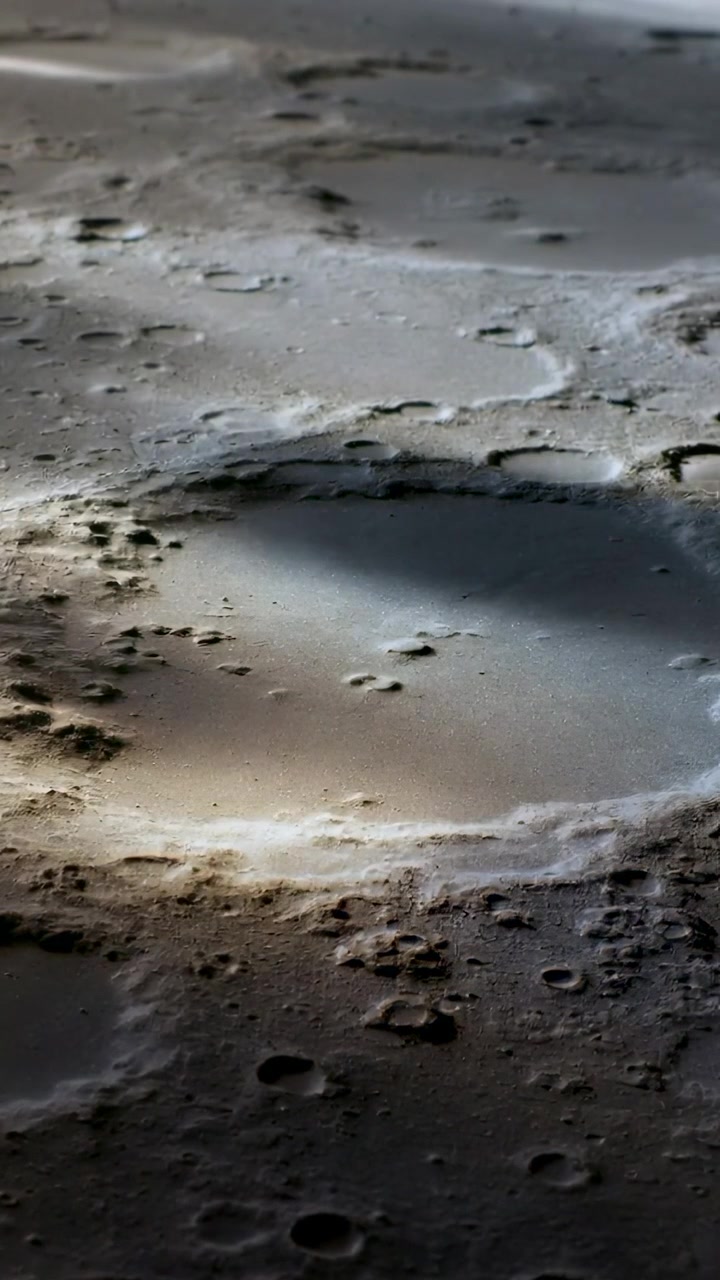 Video verticale: Telecamera che si sposta rivelando sabbia umida e granulosa sulla riva, mostrando una pozza centrale e delle fosse
