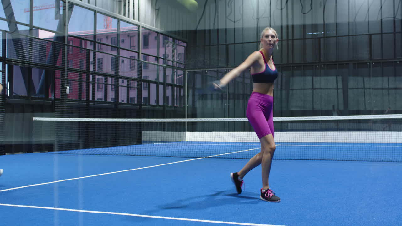 Women playing padel tennis on blue indoor court, focusing on intense match