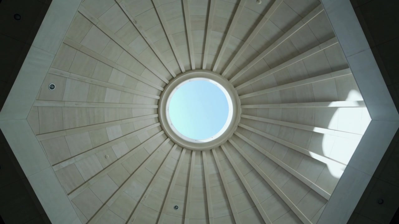 La luce solare che penetra dall'oculo crea ombre mutevoli attraverso la cupola a coste di un atrio, mettendo in risalto gli elementi architettonici.
