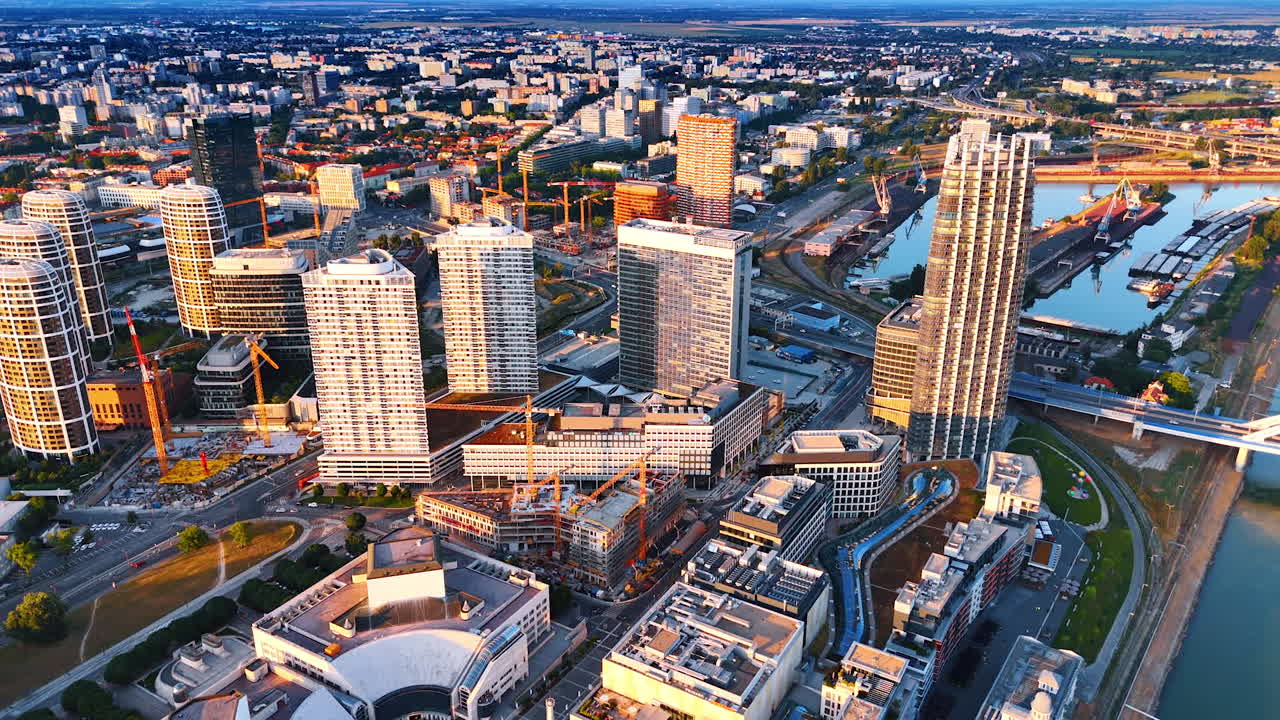 Approaching the high-rises with sunlit facades in the cityscape of Bratislava, Slovakia. Several buildings are being constructed. Aerial view