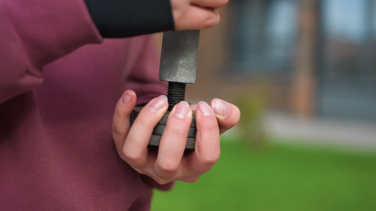 Close view of gym enthusiast hands adjusting metal dumbbell screw in outdoor setting, focus on grip and threading detail, showcasing dedication, and commitment to strength training progress