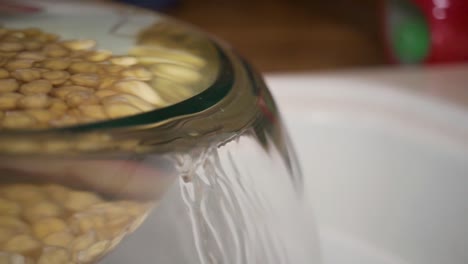 pouring water out of glass bowl with chickpeas, slow motion close up