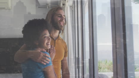 embracing couple looking out large window at home with animation on screen