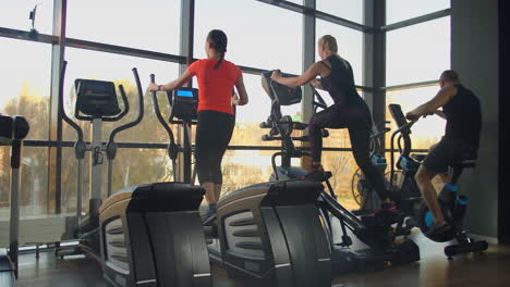 young fit woman using an elliptic trainer in a fitness center. a group of young women train on sports training equipment in a fitness gym. steady cam shot.