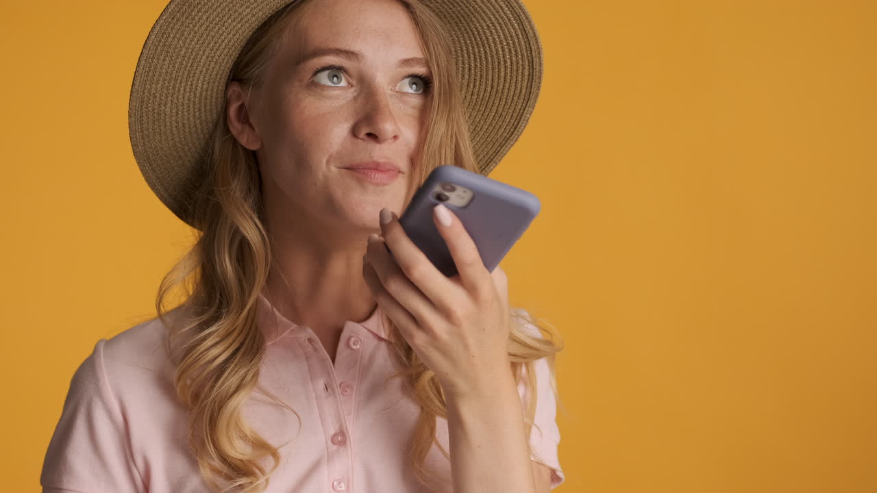 Caucasian woman in a hat recording a voice message.