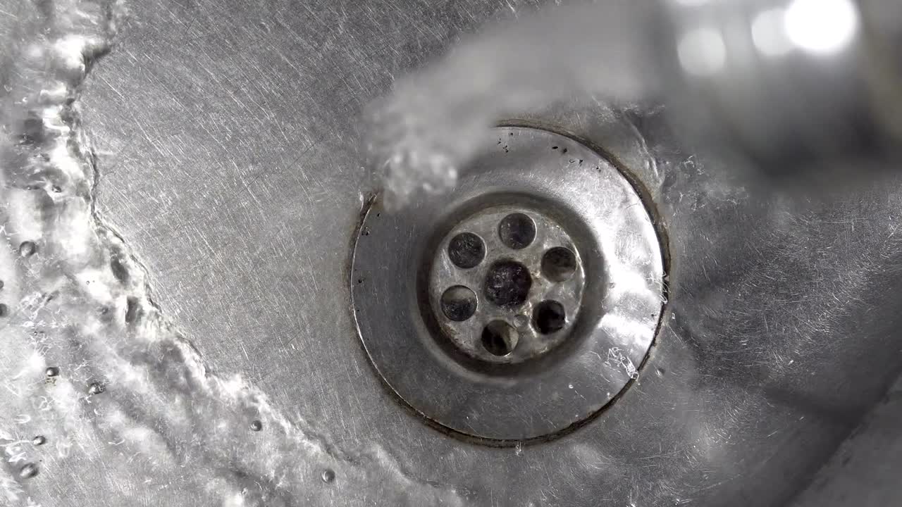 Water drops dripping and water running from a tap into a kitchen sink, cinematic background loop