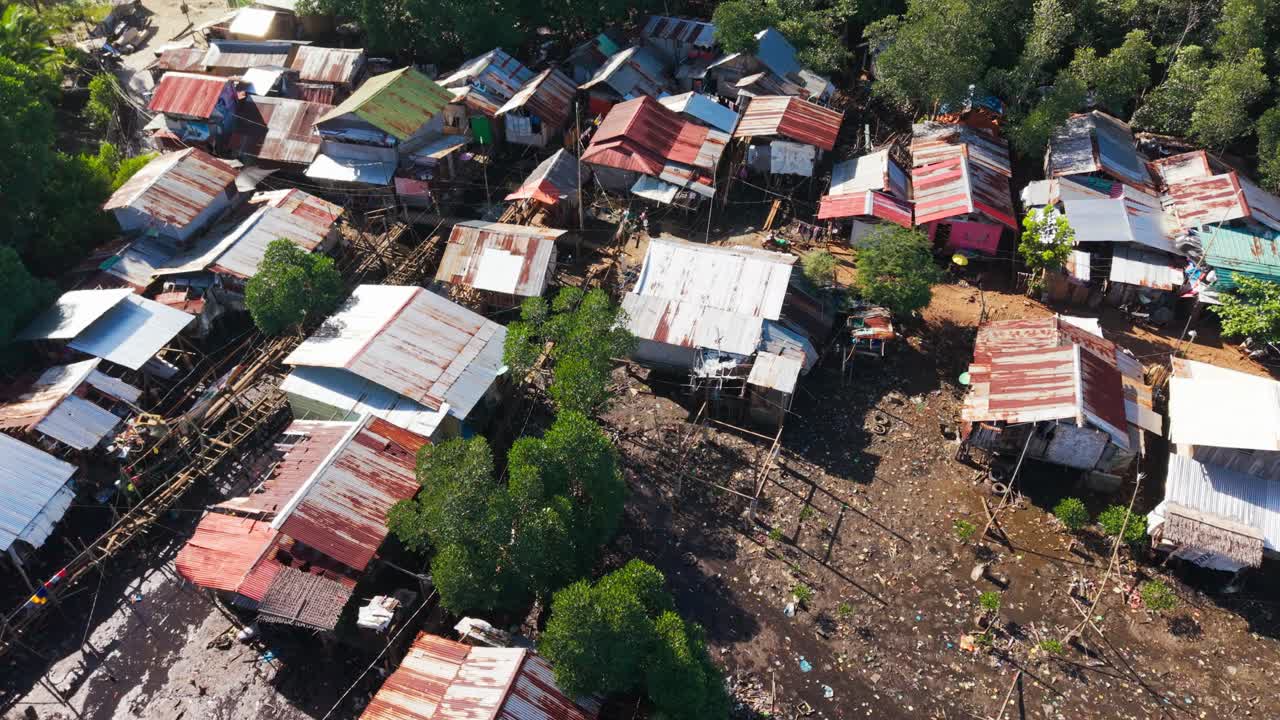 Drone svever over gjørmete, oversvømmet mark med skjøre hjem og spredte vrakrester.