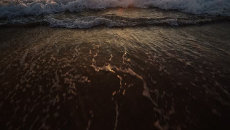sunset light reflects on the wet sand as gentle waves roll over the beach in algarve, portugal