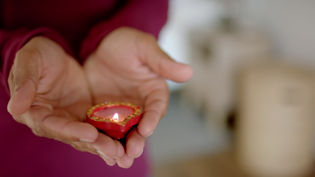 Holding lit diya, person celebrating traditional Indian festival of diwali at home