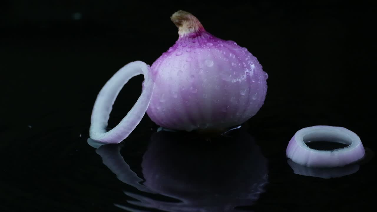 Raw onion and falling sliced rings on wet surface, black background