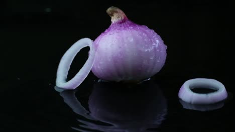 Raw-onion-and-falling-sliced-rings-on-wet-surface,-black-background