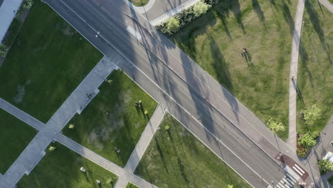 car drives on quiet road next to green park in sun, aerial drone shot