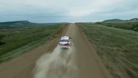 aerial view of a car racing on a dirt road through a mountainous landscape