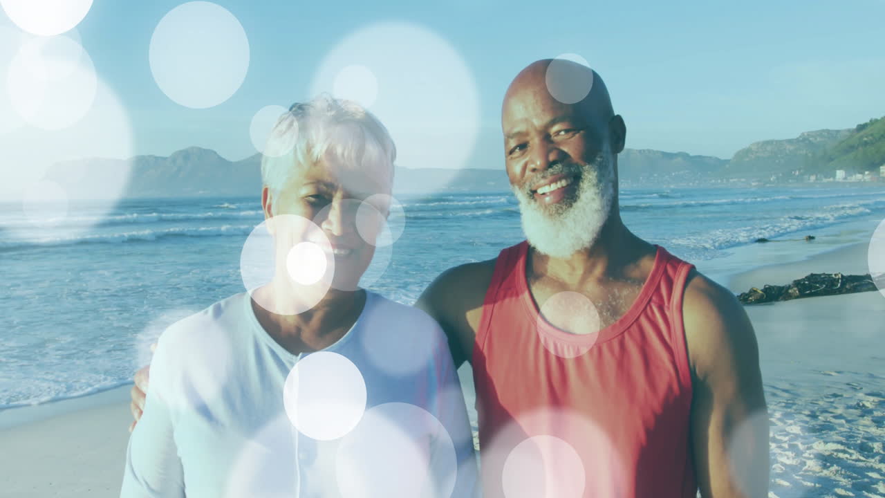 Senior couple standing at beach water edge, exploring health theme with animated light flares