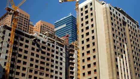 tilt up panorama of high buildings under construction in center of modern city in sunny day