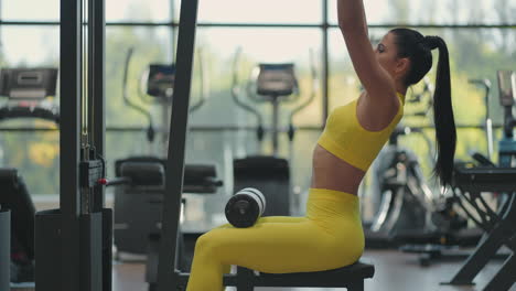 mujer hispana sentada en un simulador en el gimnasio tira de una cuerda de metal con el peso bombea los músculos de la espalda. mujer morena tira del simulador. realizando ejercicio para los músculos de la espalda simulador