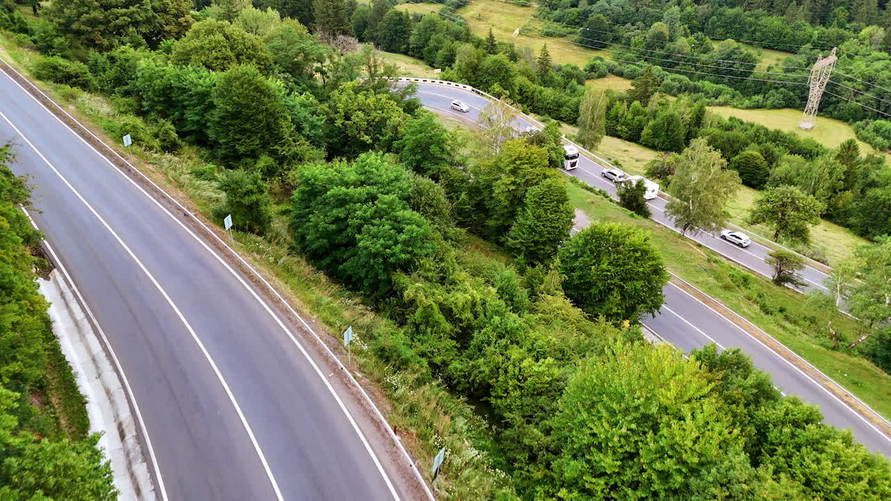 Truck on winding road through trees. A red truck drives along a curvy road surrounded by lush green trees in a scenic landscape