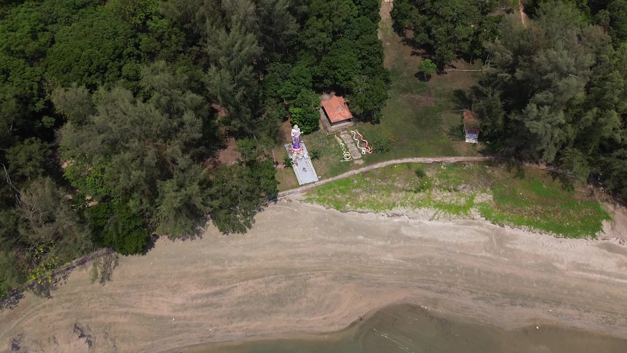 Vista aérea de um templo costeiro tranquilo na Ilha Koh Jum, Tailândia, rodeado por selva tropical e costa com praia de areia e o Mar de Andamão claro, criando uma cena de viagem serena na ilha, sem pessoas.