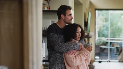 feliz pareja diversa abrazando y bebiendo café en la cocina