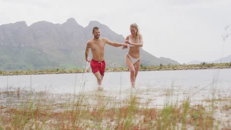 caucasian couple having a good time on a trip to the mountains, wearing bathing suits, running and j