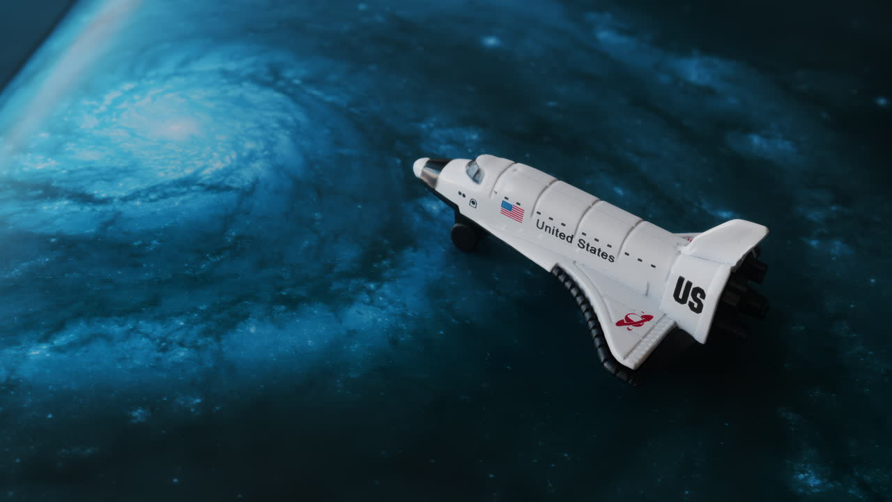 Close up of a miniature toy space shuttle placed on a blue cosmic galaxy backdrop
