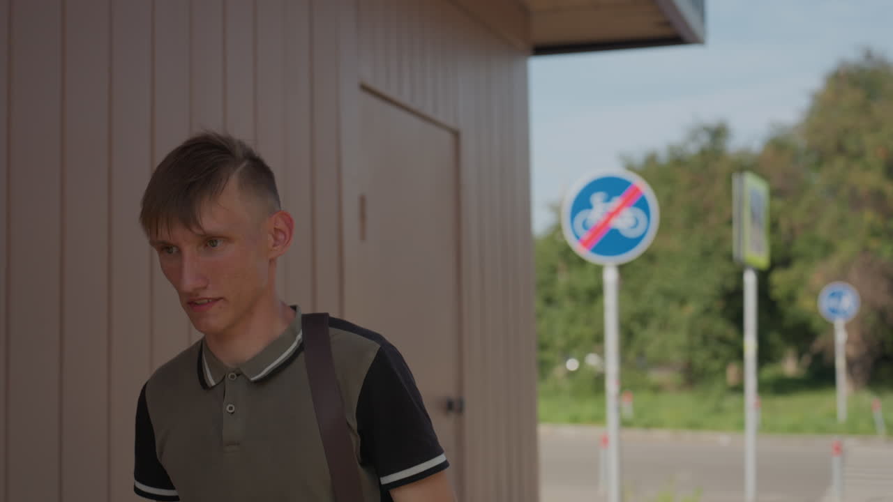 Young Caucasian Student Standing At Shelter, Sunlit Suburban Sign Visible, Backpack Strap Over Shoulder, Nervous Glance And Pensive Expression Conveying Anxiety And Paranoia Undertones