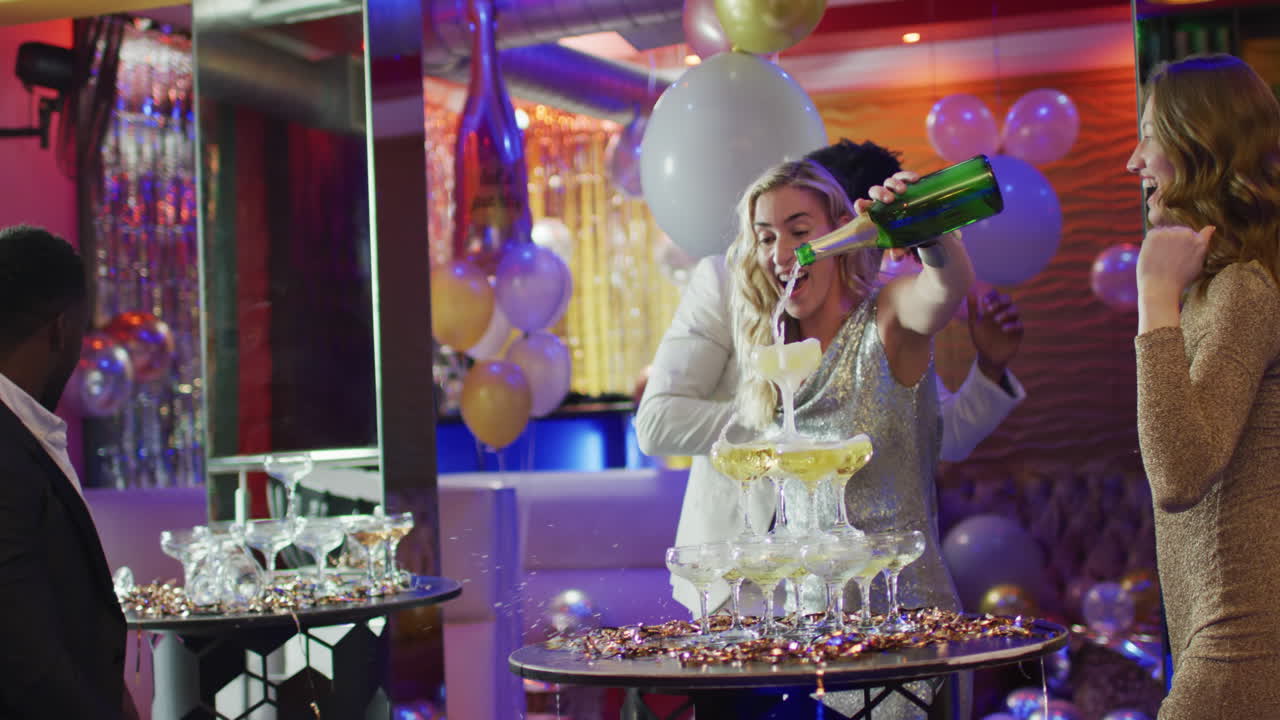 Video of happy caucasian woman pouring a champagne fountain with diverse friends at nightclub