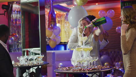 video of happy caucasian woman pouring a champagne fountain with diverse friends at nightclub