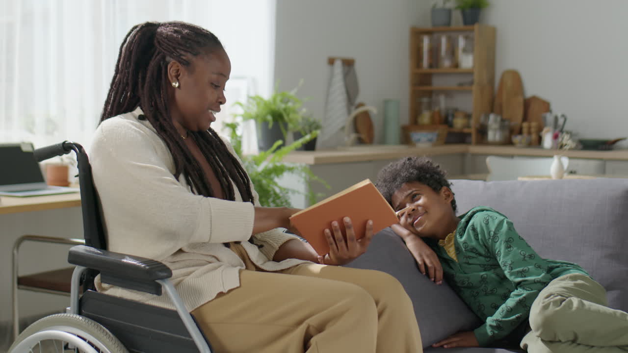 Woman in Wheelchair Reading Book to Little Son at Home