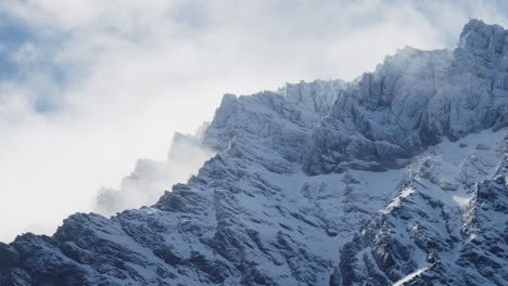 rugged snowy mountains with beautiful clouds rolling over with a blue sky